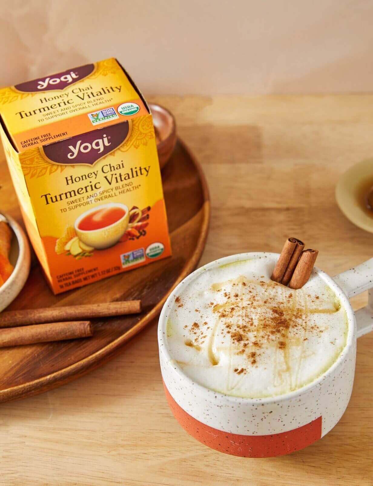 A mug of Honey Golden Milk Latte sits on a counter next to a carton of Yogi Honey Chai Turmeric Vitality Tea