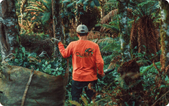 A person in an orange jacket with the word 'Quality' on the back walking through a lush forest, implying sustainable practices.