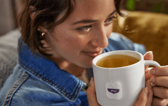Close-up of a woman smiling gently while holding a white mug with Yogi tea, indicating a moment of enjoyment.